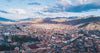 Aerial view of Cusco city center with red-roofed buildings, historic cathedral area, and surrounding Andes mountains
