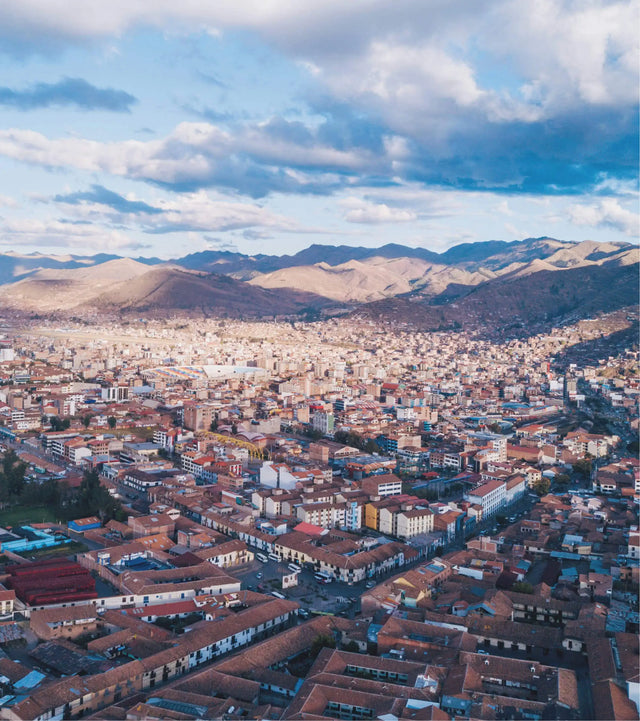 Aerial view of Cusco city showing red‑tiled roofs and streets with the Andes mountains in the background