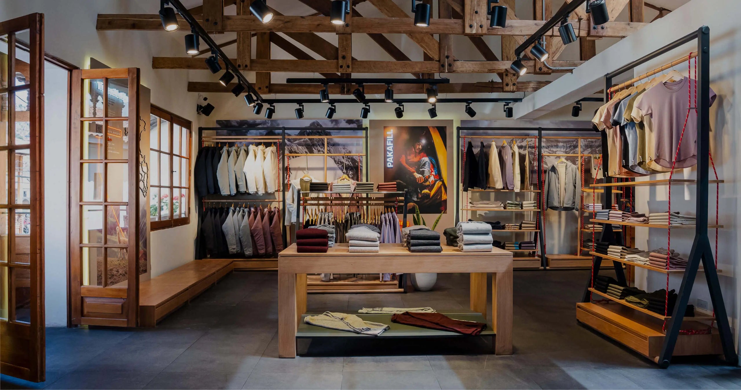 Flagship store interior with clothing displays, café counter, wooden beams, and seating area showcasing Andean textiles