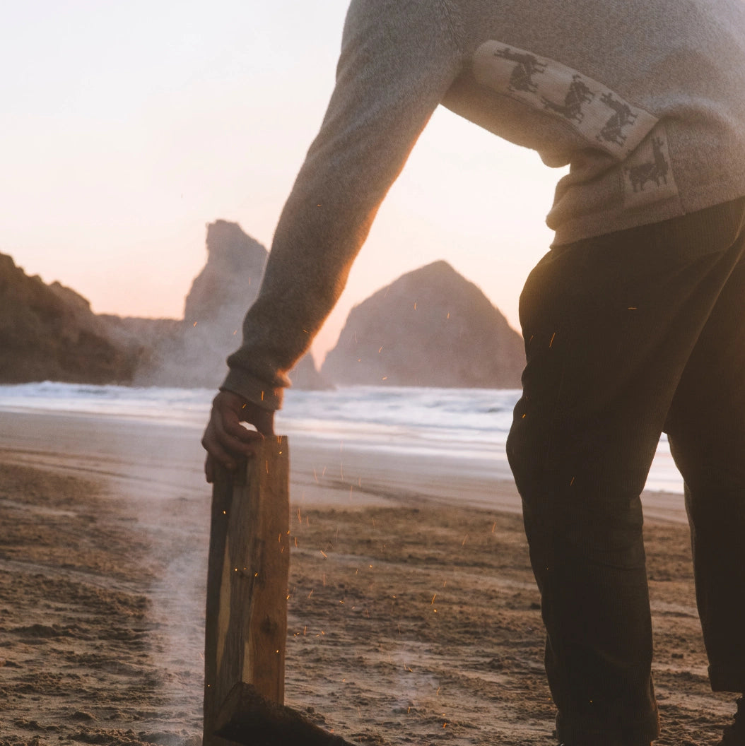 Side view of The Cusco sweater on model showcasing Inca motif panel and alpaca-merino knit at a beach sunset