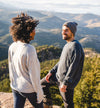 Two people wearing lightweight alpaca crew sweaters standing on a mountain overlook with a scenic valley in the background