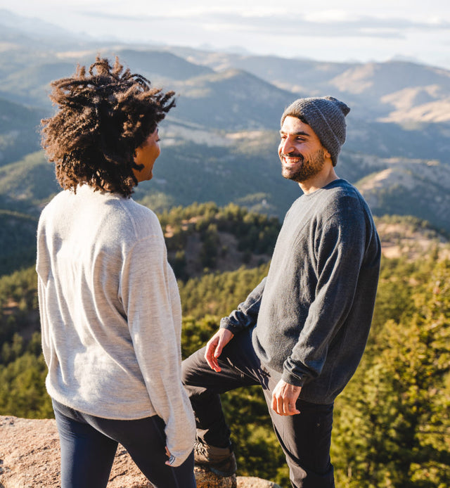 Two people wearing lightweight alpaca crew sweaters standing on a mountain overlook with a scenic valley in the background
