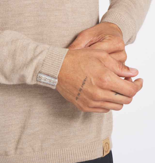 Close-up of beige Ultralight Crew sweater showing handwoven Inca ID at the wrist and leather hem tag on white background