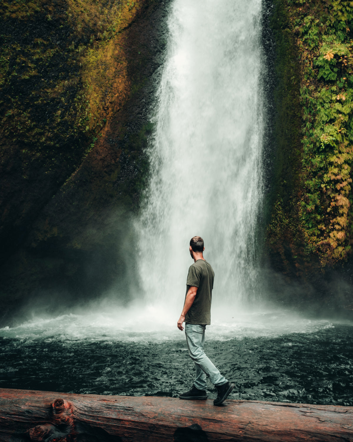 Man Named Nash Walking on Log in Front of Waterfall in Green Sustainable Alpaca T-Shirt – PAKA Apparel