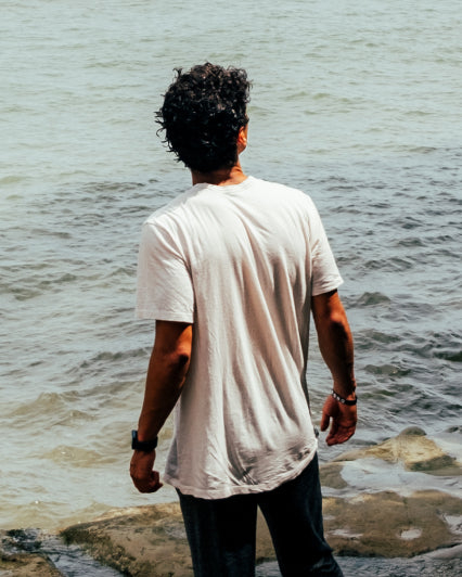 Back of Man Named Sebastian in White Alpaca T-Shirt in Front of Ocean – PAKA Apparel