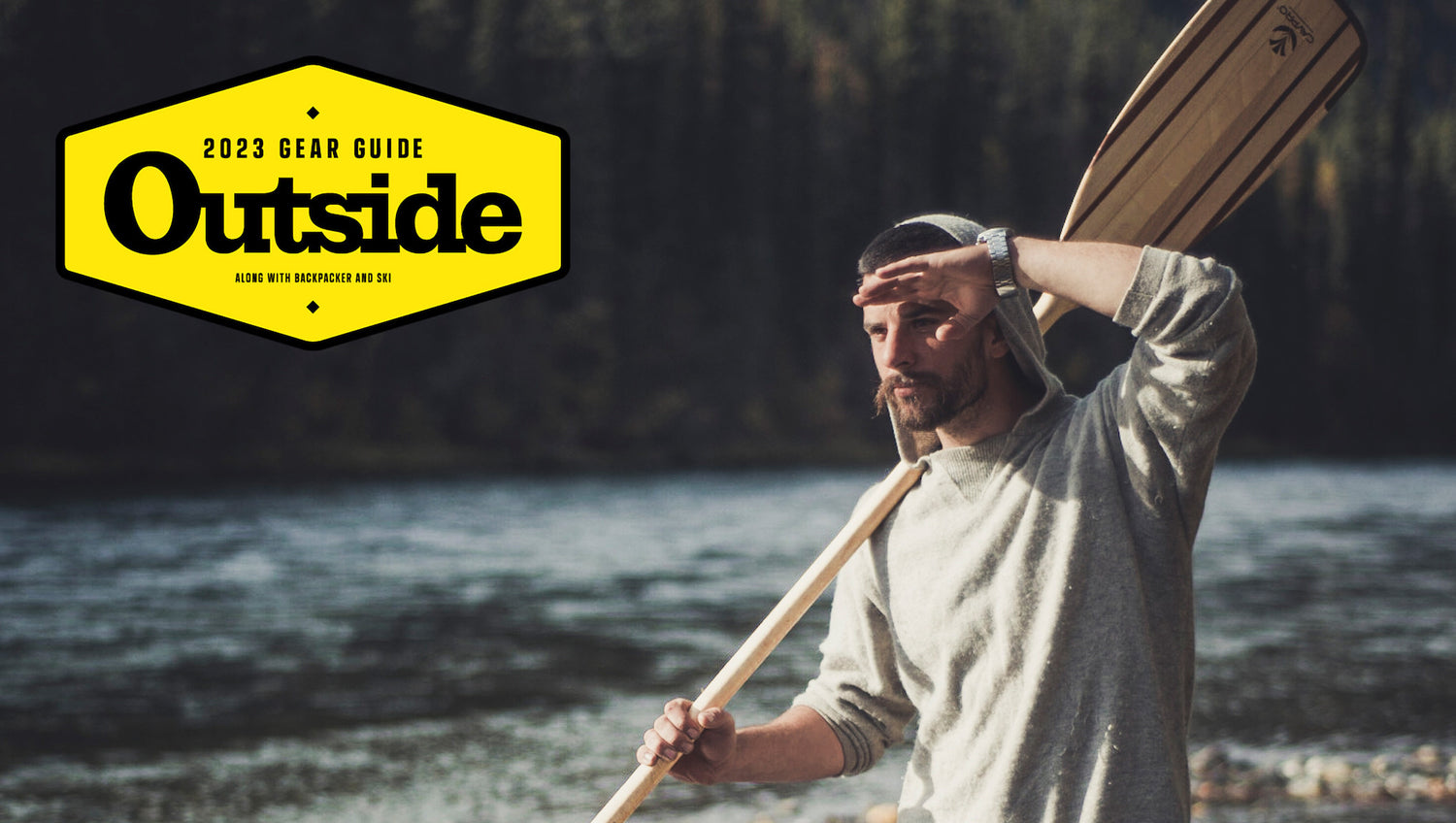 Man Holding Wood Paddle by River in The Hoodie Light Grey Hooded Sweater with 2023 Outside Magazine Gear Guide Logo Overlay – PAKA Apparel