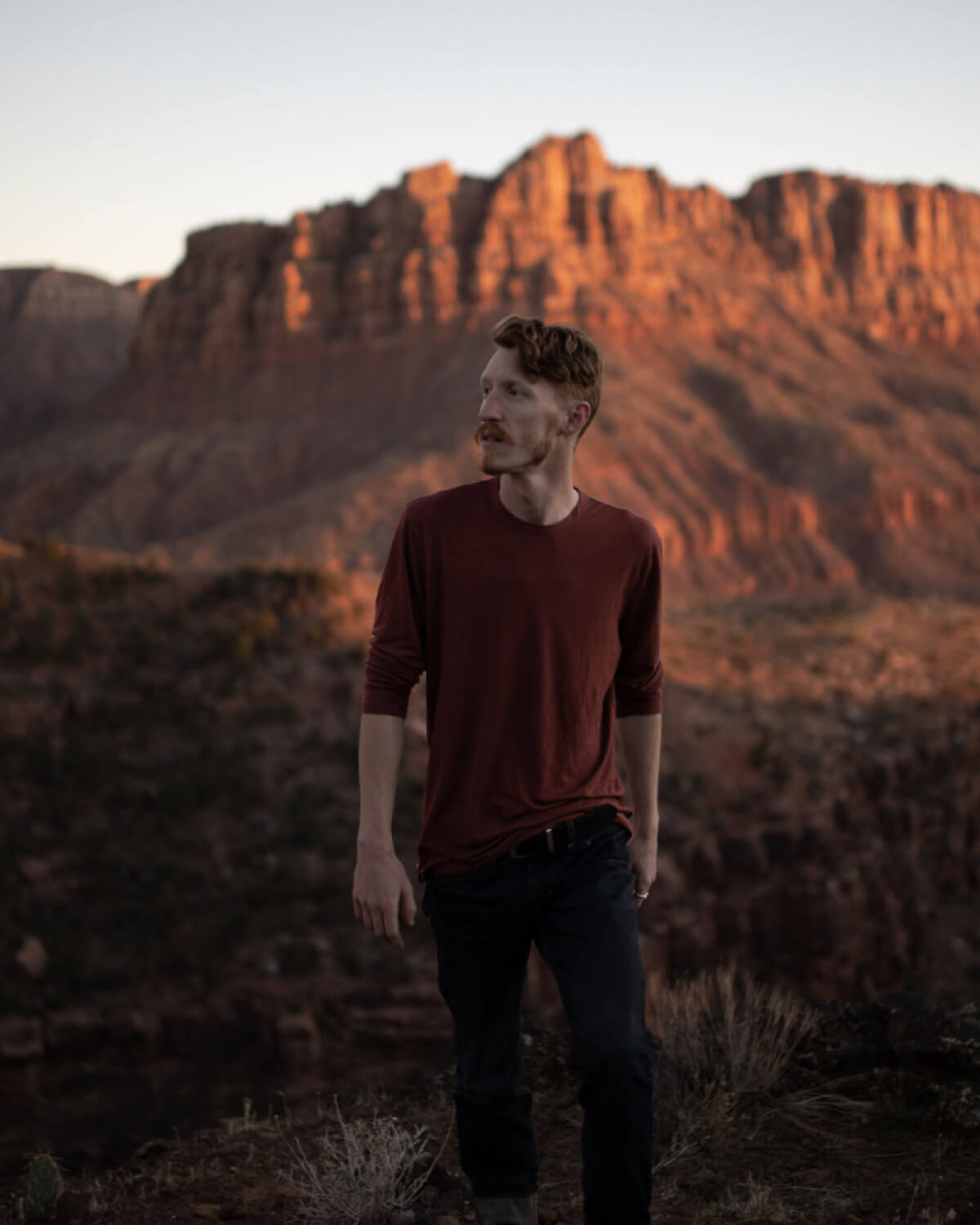 Man Named Josh Wearing Clay / Red Aire Long Sleeve Shirt in in Front of Vast Red Rock Canyon – PAKA Apparel