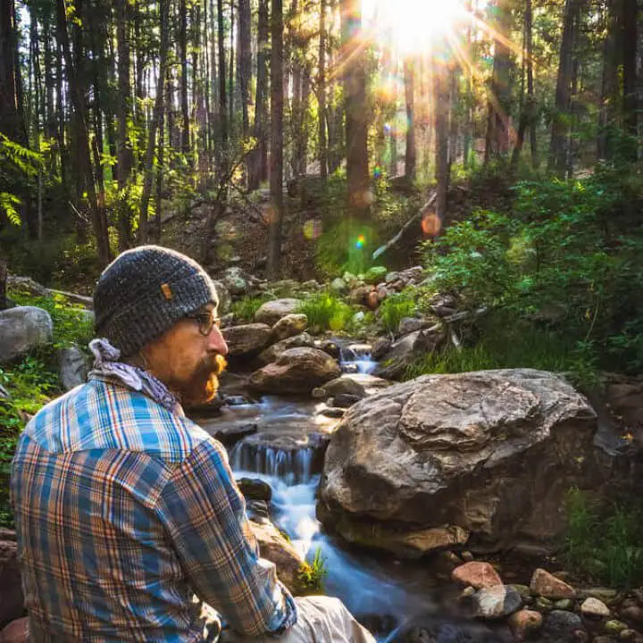 A man in a plaid shirt with his alpaca beanie in front of a river 