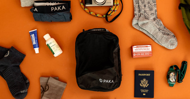 Black upcycled packing cube surrounded by travel items on orange background