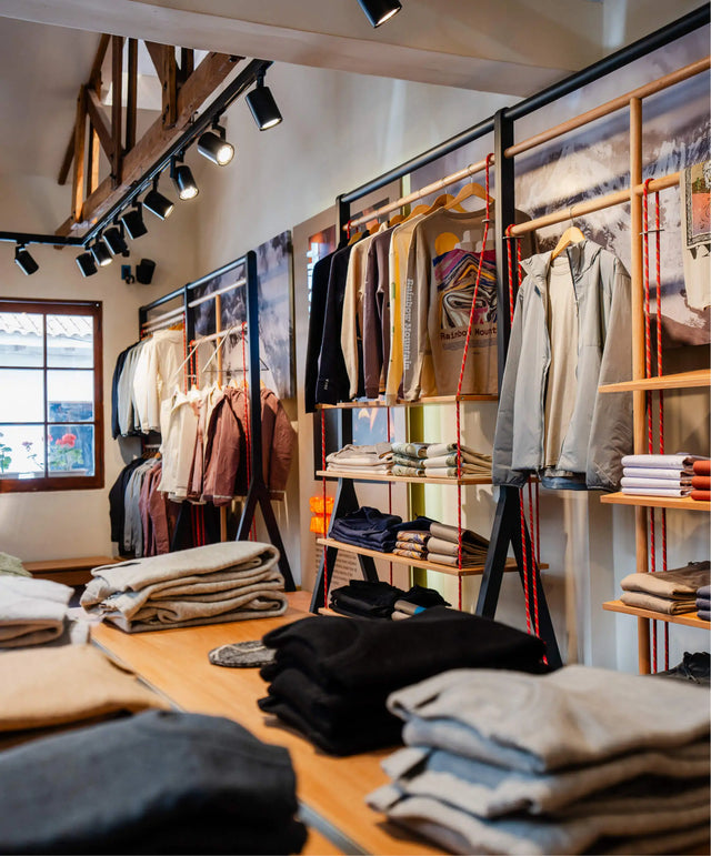 Paka store interior with folded sweaters and hanging jackets on wooden tables and rope-suspended racks under track lighting