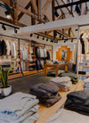Clothing store interior with exposed wooden ceiling beams, folded sweaters on tables and jackets hanging on racks