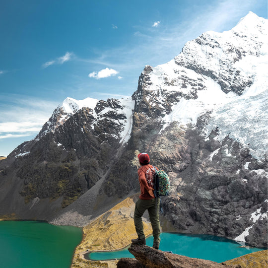 A man looking at the snowy Ausangate Mountain and a mineral blue lake