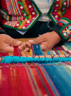 Woman weaving a colorful striped textile by hand, close-up of hands and embroidered clothing