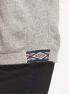 Close-up of sweater hem showing woven Inca ID tag with geometric red and navy pattern against black pants