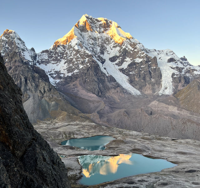 The mountain Ausangate with a blue glacial lake at it's base reflecting the mountain in the sunlight. 