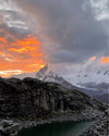 Yanapaccha peak at sunset with glowing orange sky, heavy clouds, rocky moraine and a glacial lake in the foreground