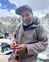Climber preparing ropes and carabiners while wearing a fleece jacket on a rocky glacial slope near snowy peaks
