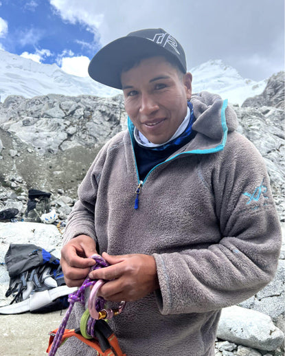Climber preparing ropes and carabiners while wearing a fleece jacket on a rocky glacial slope near snowy peaks