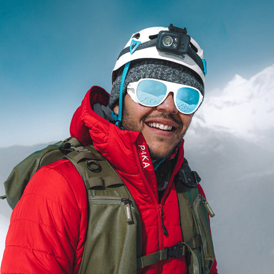 Mountaineer in red jacket and goggles standing on a snowy mountain ridge with cloudy sky behind