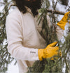 Person wearing a cream PAKACLOUD fleece and yellow knit gloves arranging pine branches outdoors