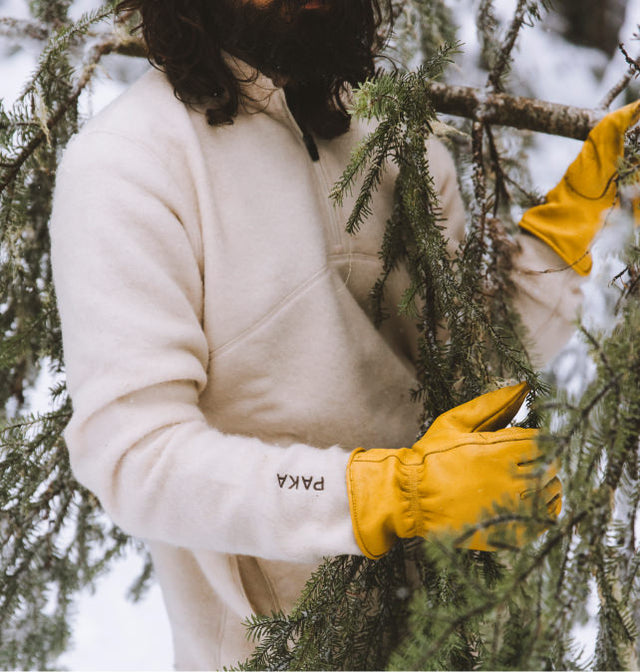 Person wearing a cream PAKACLOUD fleece and yellow knit gloves arranging pine branches outdoors
