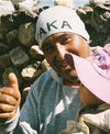 Man smiling and giving a thumbs-up while holding a child in a pink sun hat against a rocky mountain background