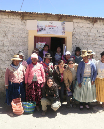 PAKA team member, Gisella, posing with a group of local Quechua women outside a stone building in Peru
