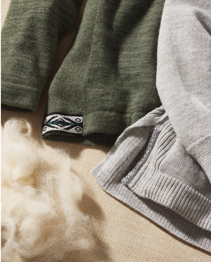 Close-up of two women’s hoodies (olive and light gray) showing woven hem detail and alpaca fiber on a beige fabric background