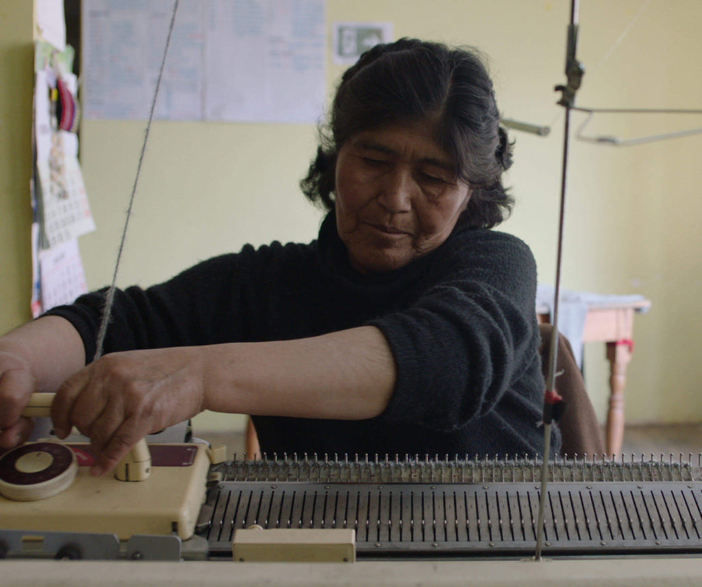 Woman operating a flatbed knitting machine in a workshop, threading yarn through the needles