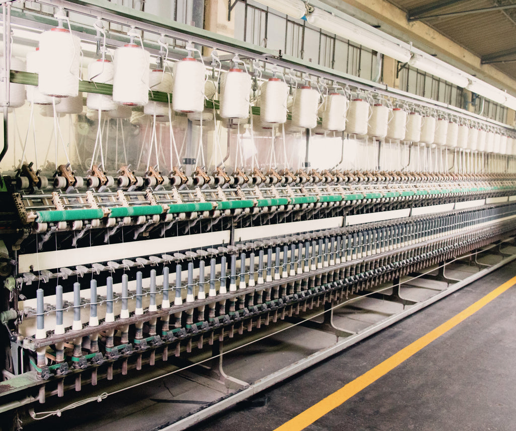 Rows of industrial spinning machines winding alpaca fiber into yarn on dozens of white spools in a mill