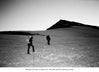 Two climbers walking across a snowy slope toward a distant mountain peak in a high-altitude landscape