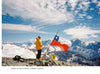 Two climbers on a snowy summit holding a Chilean flag with mountains and sky behind them