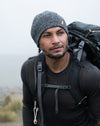 Hiker wearing a gray knit beanie and black jacket carrying a backpack on a foggy mountain trail