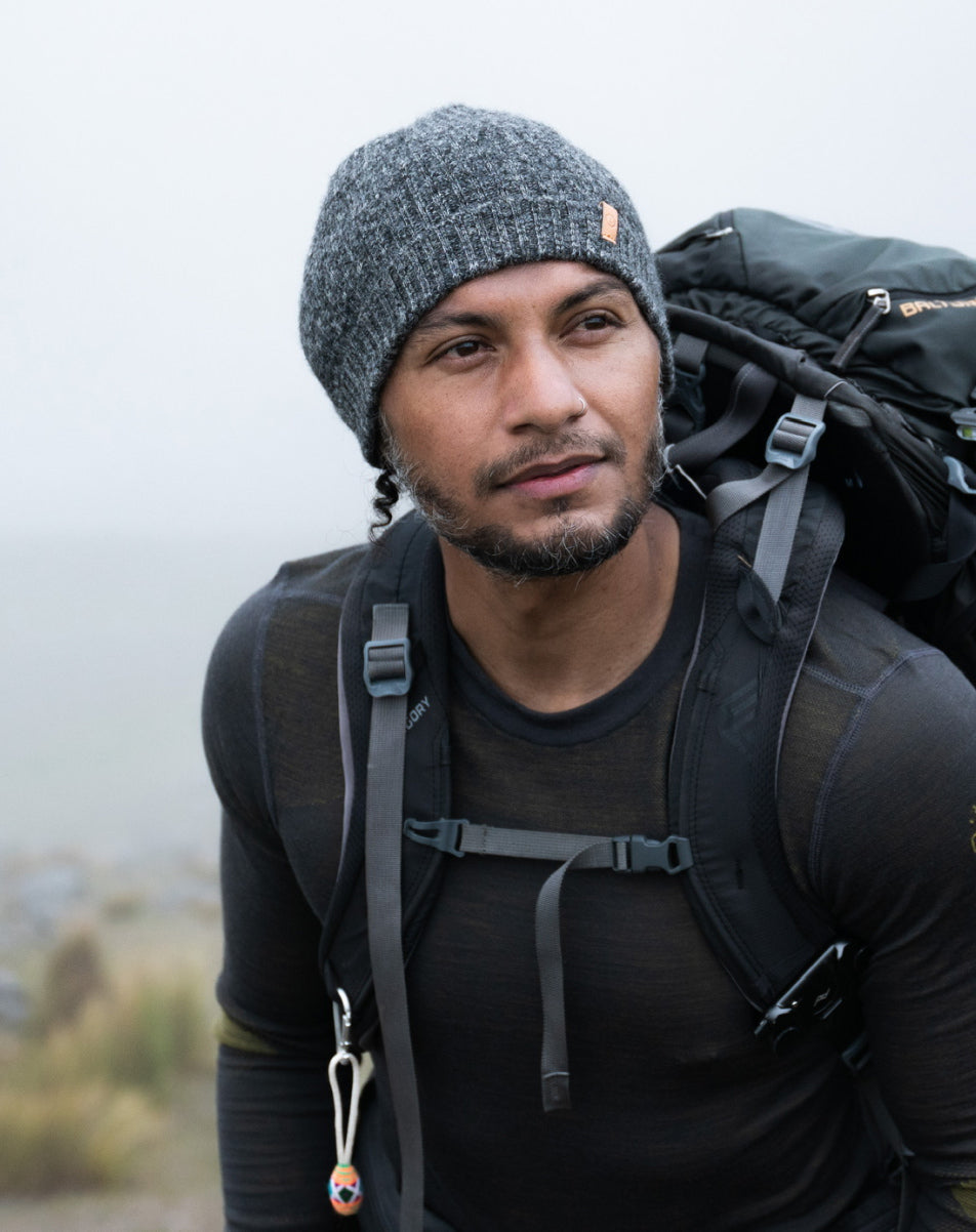 Hiker wearing a gray knit beanie and black jacket carrying a backpack on a foggy mountain trail