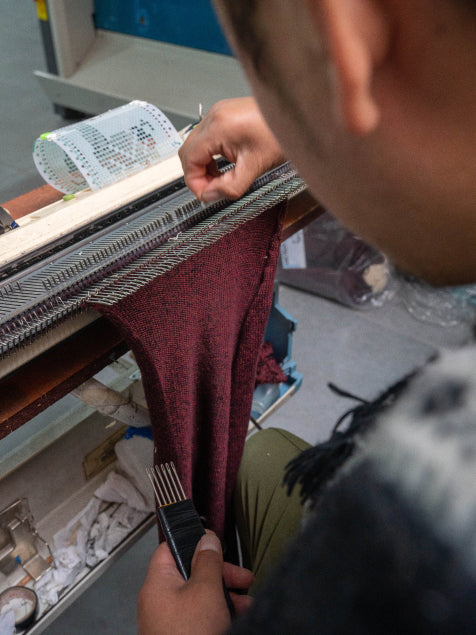 Artisan knitting maroon Vida sweater fabric on a flatbed knitting machine in a workshop