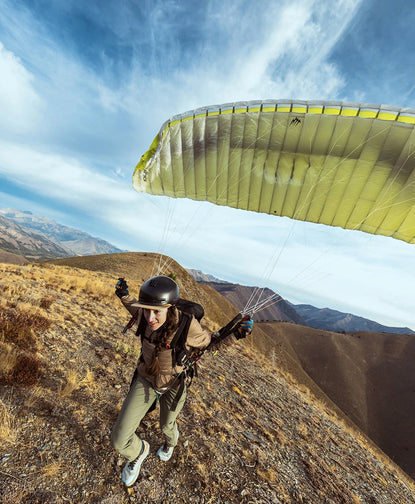Hiker wearing Mayu ultralight PAKAFILL jacket preparing to paraglide on a windswept hillside