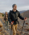 Two hikers wearing black Mayu ultralight alpaca jackets hiking on a mountain trail, one using trekking poles