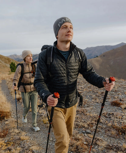 Two hikers wearing black Mayu ultralight alpaca jackets hiking on a mountain trail, one using trekking poles
