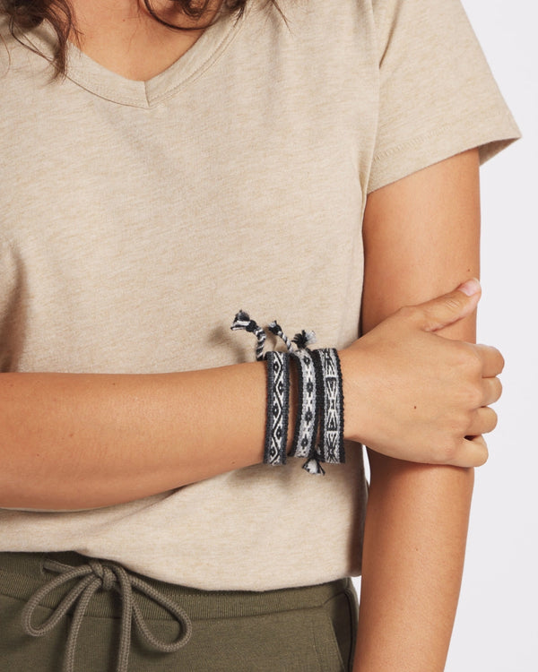 Close-up of wrist wearing three handwoven Quechua alpaca bracelets with black-and-gray geometric Inca pattern on neutral background