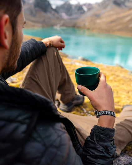 Man Drinking Coffee in Front of Lake Wearing Ñawi Grey Handwoven Quechua Alpaca Bracelet – PAKA Apparel