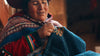 Indigenous woman wearing colorful handwoven Andean textiles, seated portrait in warm natural light