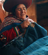 Indigenous artisan weaving a colorful traditional textile indoors, wearing a patterned poncho and hat