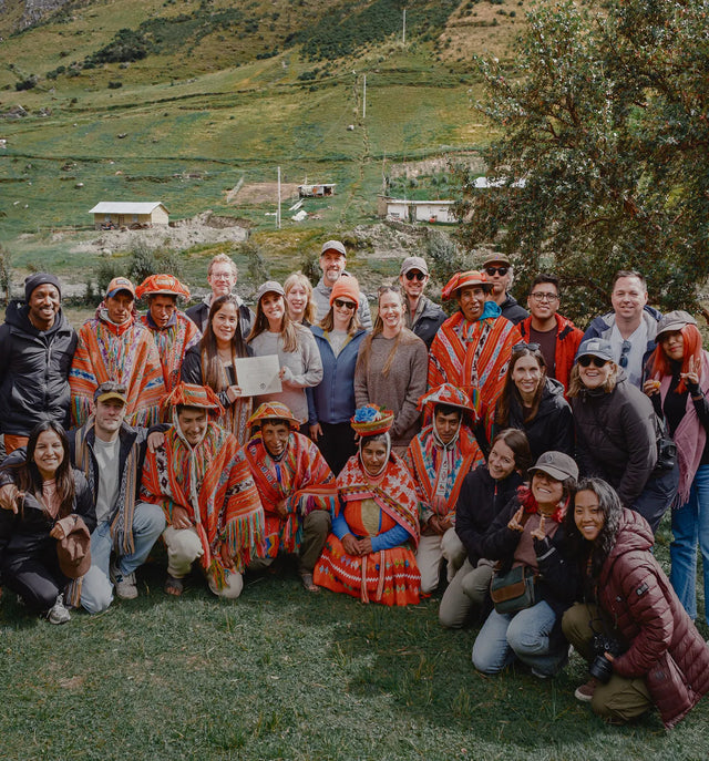 Group of PAKA team members and Quechua weavers posing together on a grassy Andes hillside near Cusco