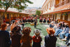 Group of people gathered in a sunlit Cusco market courtyard surrounded by colorful textiles and colonial-style buildings