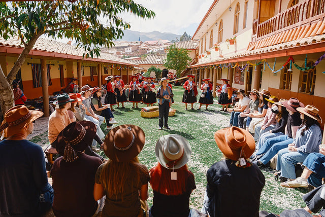 Group of people gathered in a sunlit Cusco market courtyard surrounded by colorful textiles and colonial-style buildings