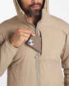 Front torso view of Apu Lightweight Puffer in sand showcasing zippered chest pocket holding a smartphone, hood up