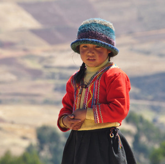 Woman in red traditional Peruvian clothing standing outdoors with mountains in the background