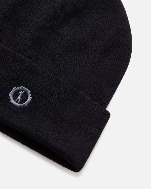 Angled close-up of black cuffed beanie showcasing embroidered PAKA logo on alpaca wool cuff against light gray background