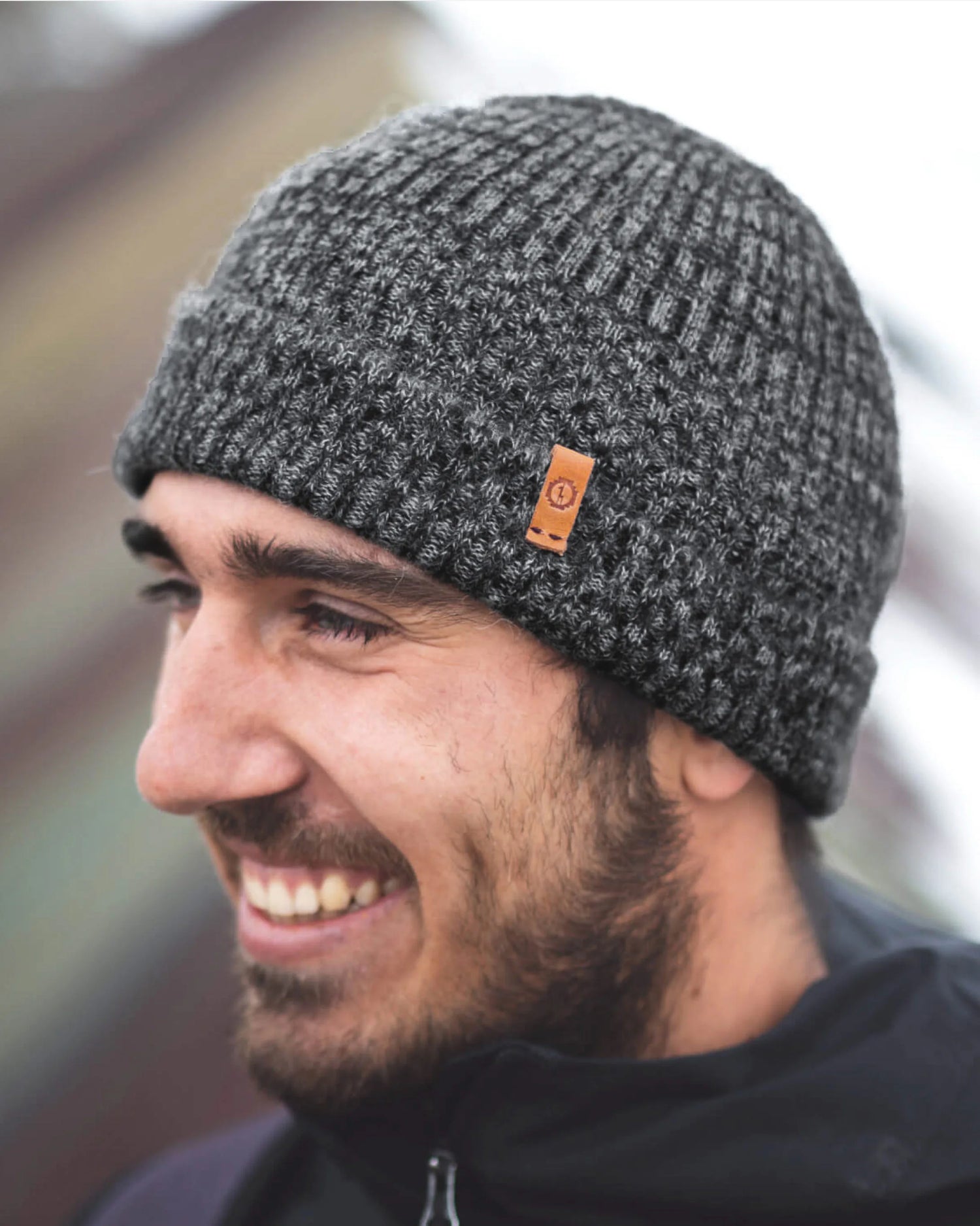 Side view of model wearing Cozy Marled Beanie in charcoal showcasing marled rib knit, folded cuff, and leather logo tag