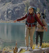 Model wearing Mayu ultralight jacket standing on a rocky lakeshore with lake and mountains in the background